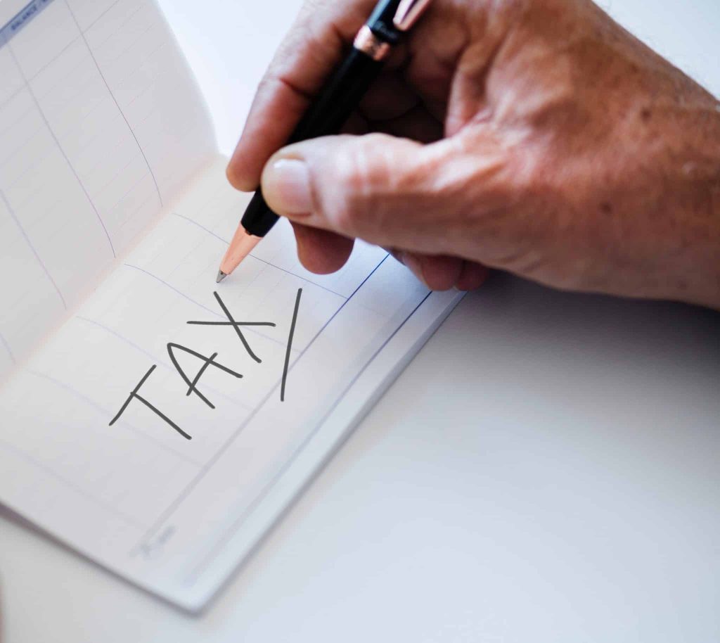 Hand with pen writing the word tax on a note card