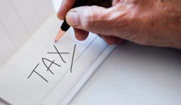 Hand with pen writing the word tax on a note card
