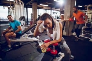 woman in workout clothes wiping her forehead with a cloth at the gym