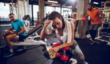 woman in workout clothes wiping her forehead with a cloth at the gym