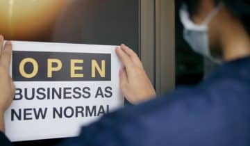 Reopening for business adapt to new normal in the novel Coronavirus COVID-19 pandemic. Rear view of business owner wearing medical mask placing open sign